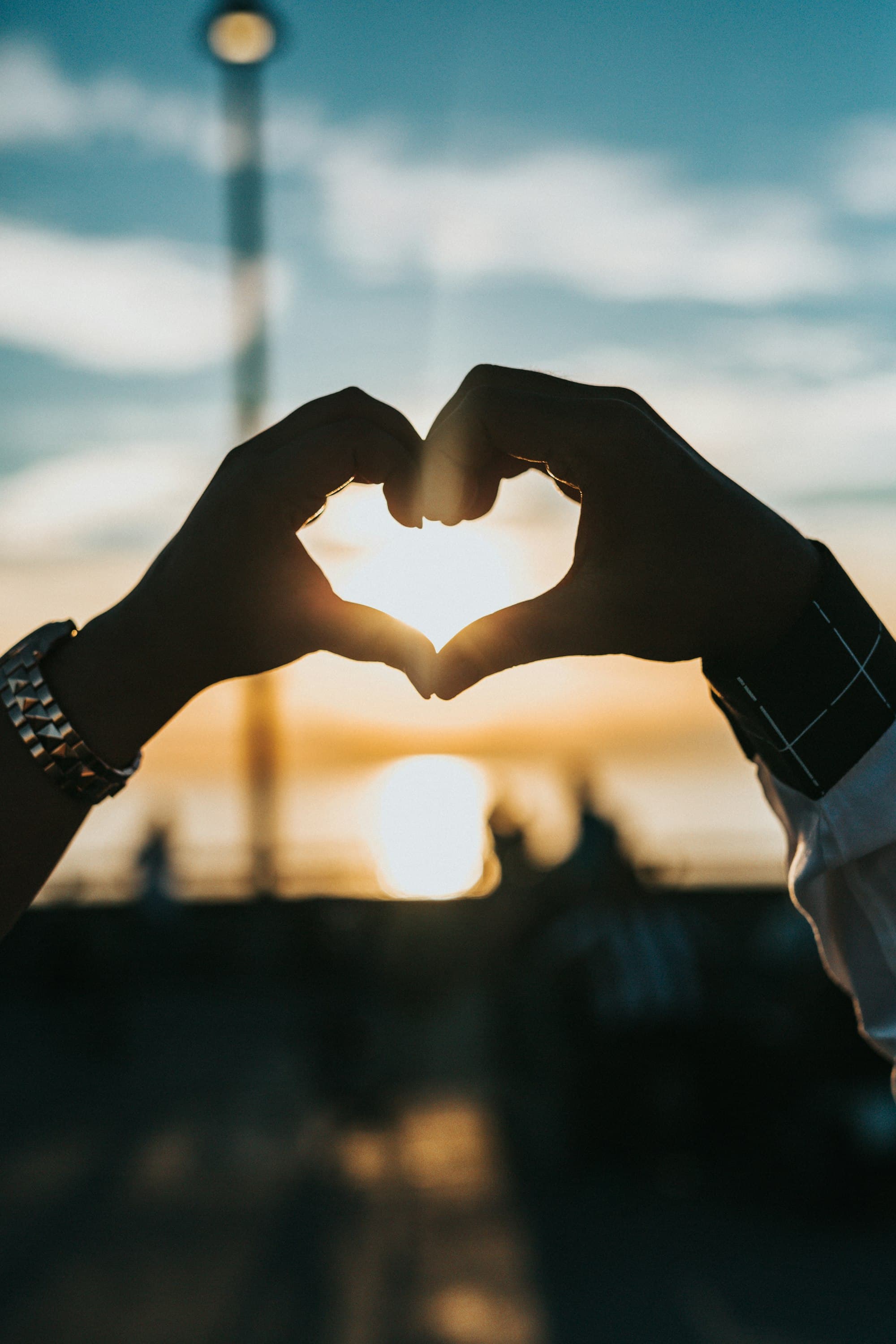 Hands forming a heart against a sunset sky